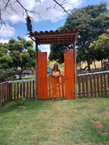 Eine Frau sitzt in einem Tor in einem Zaun in der Unterkunft Chácara Belas Artes in Sairé