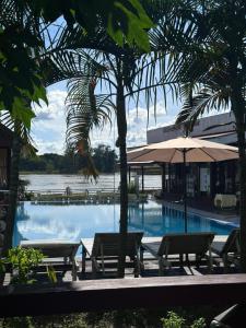 a pool with benches and an umbrella next to a building at golden hotel dondet in Don Det