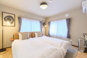 a bedroom with a large white bed with windows at Casa Katatsumuri in Nakafurano