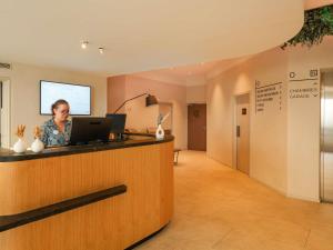 a woman is standing at a counter in a waiting room at Mercure Colmar Centre Unterlinden in Colmar