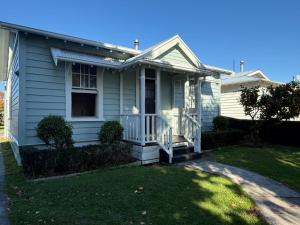 Hawke's Bay Escape - Railway Cottage في هاستينغز: منزل أبيض مع شرفة وساحة
