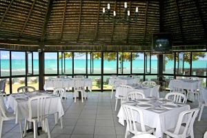a restaurant with white tables and chairs and the ocean at Baia Cabralia Hotel in Santa Cruz Cabrália