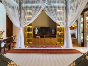 a bedroom with a bed with curtains and a television at Des Indes Villas in Seminyak