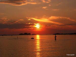 a sunset on the water with a boat at Capitol Apartments in Grado