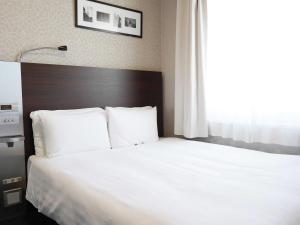 um quarto com uma cama com lençóis brancos e uma janela em Comfort Hotel Tokyo Higashi Nihombashi em Tóquio
