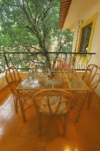 a glass table and chairs on a balcony with a tree at Navilehomestay in Candolim