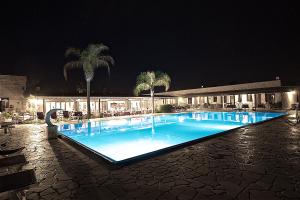 a swimming pool at night with palm trees and a building at Hotel Masseria Le Pajare in Presicce
