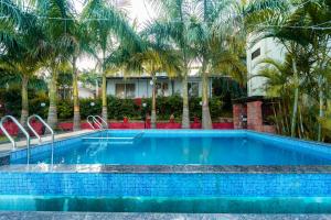 a swimming pool with palm trees in front of a house at Strawberry County in Panchgani