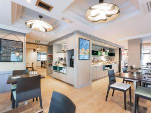 a restaurant with tables and chairs and a kitchen at Mercure Grenoble Centre Porte des Alpes in Grenoble