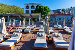 eine Gruppe von Liegestühlen mit Sonnenschirmen am Strand in der Unterkunft Hotel Riva by Aycon in Petrovac na Moru