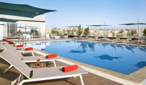 a pool on the roof of a building with lounge chairs at The Abdali Boulevard Hotel in Amman