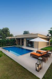 a swimming pool with an umbrella and a house at The Oberoi Vindhyavilas Wildlife Resort, Bandhavgarh in Tāla