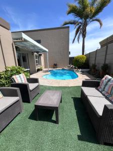 a patio with chairs and a pool with a palm tree at AquaPalms Hideaway - Family Friendly Pool - Hot Tub - Indoor Braai in Cape Town