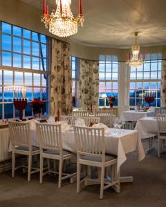 una sala da pranzo con tavoli e sedie bianchi e finestre di Ombergs Turisthotell a Ödeshög