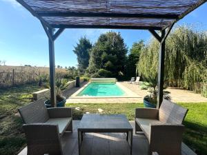 Un patio con mesa y sillas y una piscina. en La Maison Labonnechose - Piscine chauffée - Calme - Jeux, en Notre-Dame-de-Fresnay