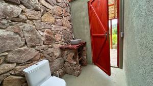 Casa Gaucho hospedate en una reserva natural في Aiguá: حمام بجدران حجرية مع مرحاض وباب أحمر +38 صورة