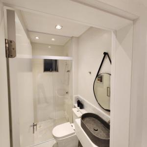 Un baño con lavabo, inodoro y espejo. en Doce lar, en Itapema