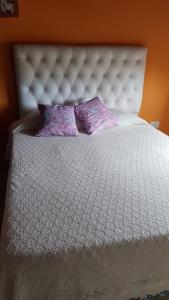Una cama blanca con dos almohadas moradas. en Departamento villa Gesell con pileta, en Villa Gesell