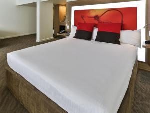 a large white bed with red and black pillows at Novotel Sydney West HQ in Rooty Hill +40 photos