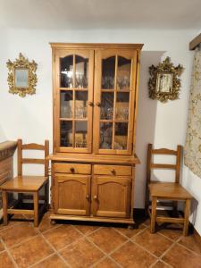 Un armario de madera con puertas de cristal y dos sillas. en La Casita de Marisol, en El Real de la Jara