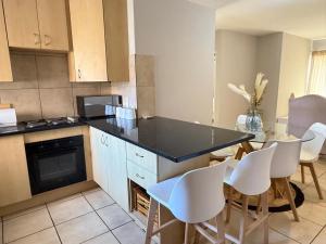 a kitchen with a black counter top and white chairs at Kloppenheim Sectional Lifestyle Complex in Ellisras