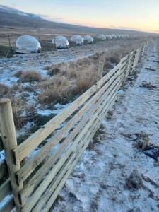 a wooden fence in a snowy field with domes at Aurora Igloo North in Hvammstangi