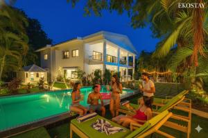 um grupo de pessoas sentadas em cadeiras à beira de uma piscina em frente a uma casa em Ekostay Luxe - CASA SIA - Ideal for Big Groups- Poker Table em Lonavala