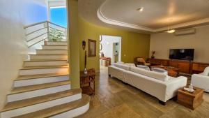 Una sala de estar con muebles blancos y una escalera. en Mansão Pé na Areia no Condomínio Cocanha, en Água Boa