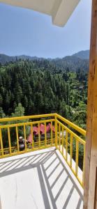 a yellow railing on a balcony with a view of trees at woodstock villa & cafe in Jibhi