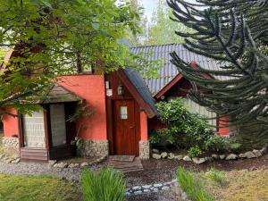 a red house with a wooden door in a yard at Casa Los Coihues in Villa La Angostura