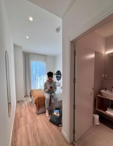 un hombre sentado en una cama en una habitación de hotel en Aparto Diagonal Suites, en Esplugues de Llobregat