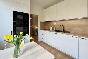 a kitchen with white cabinets and a vase of yellow flowers at Lumen apartmán in Komárno
