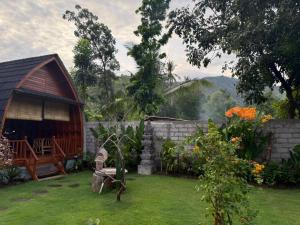 a garden with a barn and a stone wall at Qchen Cuan Cabin Amed in Amed