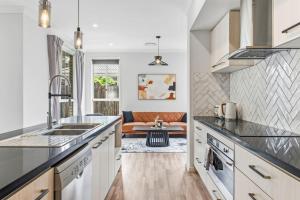 Modern Family Home in Peaceful Pallara 4BR Comfort في Algester: مطبخ مع قمم منضدة سوداء وغرفة معيشة