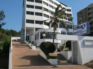 a white building with a palm tree in front of it at La Mercy Beach Hotel in La Mercy