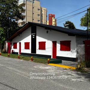 un edificio blanco con puertas rojas en una calle en Complejo Quimey No se alquila a jóvenes y se reserva con el 30 porciento del total mediante depósito bancario, en Villa Gesell