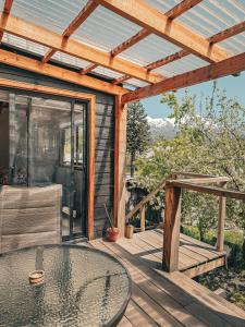 Una terraza de madera con una mesa de cristal y una pérgola. en Cabaña con vista al volcán, en Neltume