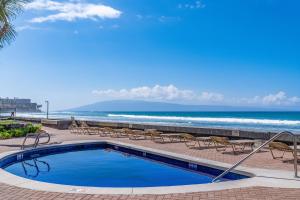 a swimming pool next to a beach with chairs and the ocean at Kulakane 304 in Kahana