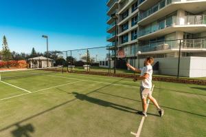 Een man die een tennisbal slaat op een tennisbaan. bij Talisman Beachside Broadbeach in Gold Coast