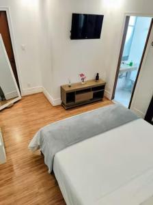 a white room with a bed and a television at Quarto-Suíte Serra Petrópolis in Petrópolis