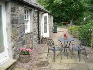 Cosy cottage for two in the highlands في Fortingall: طاولة وكراسي أمام منزل حجري