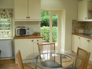 Cosy cottage for two in the highlands في Fortingall: مطبخ مع طاولة زجاجية مع كراسي وميكروويف