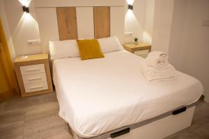 Un dormitorio con una cama grande con sábanas blancas y almohadas amarillas. en Apartamentos Palma del Río CAROLA, en Linares