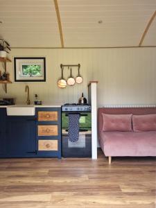 a kitchen with a stove and a pink couch at The Shepherd's Hut at Hidden Wood Glamping in Corsley