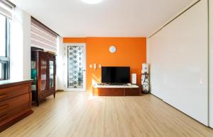 a living room with an orange wall and a flat screen tv at Paju Gallery Café Pension Soon in Paju