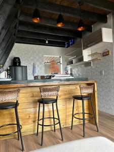 a kitchen with three bar stools at a counter at Chalé do Campo in Sumidouro