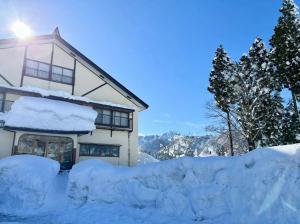 a house covered in snow with trees and mountains at ロッヂ 雪ん子 in Yuzawa