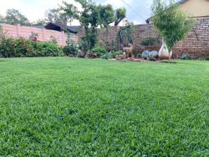 een tuin met groen gras en een stenen muur bij Highway Haven in Stilfontein