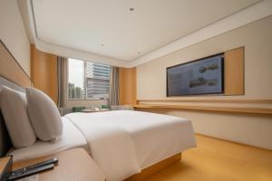 een slaapkamer met een wit bed en een flatscreen-tv bij JI Hotel Chengdu Qingbaijiang Phoenix Lake in Chengdu