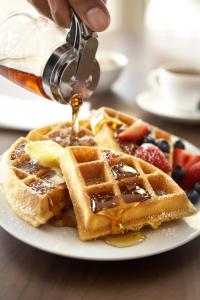 a person is pouring syrup onto a plate of waffles at Country Inn & Suites by Radisson, Mason City, IA in Mason City